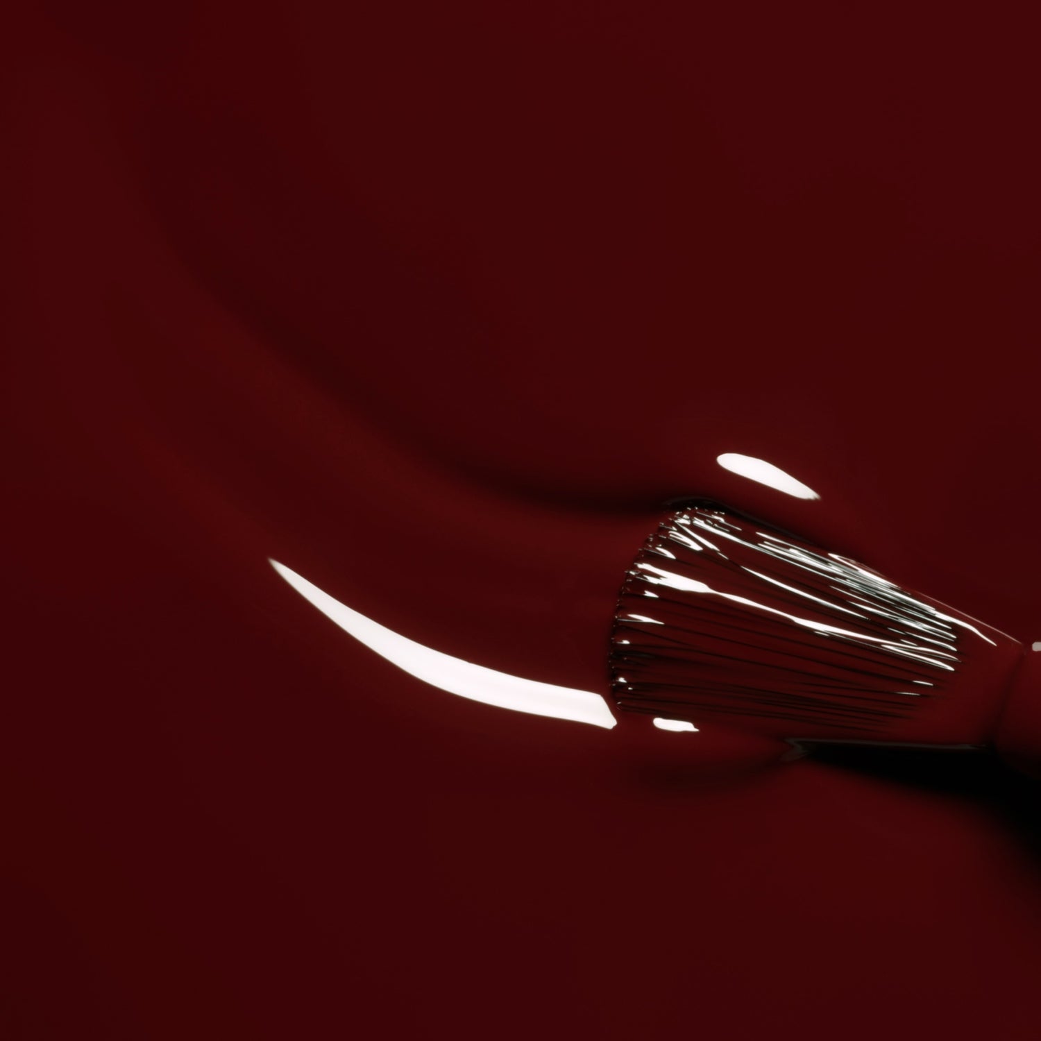 A close-up of a brush applying Manucurist’s Grenat gel polish—a glossy maroon red—while light reflects on its smooth, wet surface.