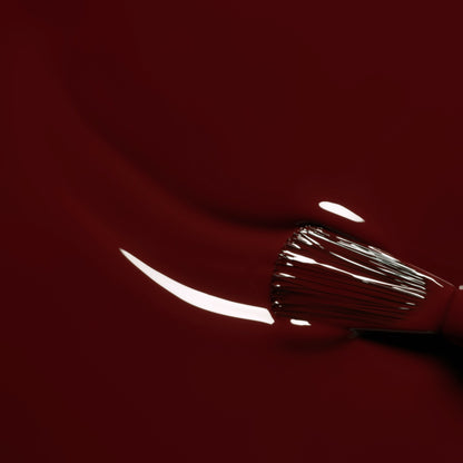 A close-up of a brush applying Manucurist’s Grenat gel polish—a glossy maroon red—while light reflects on its smooth, wet surface.