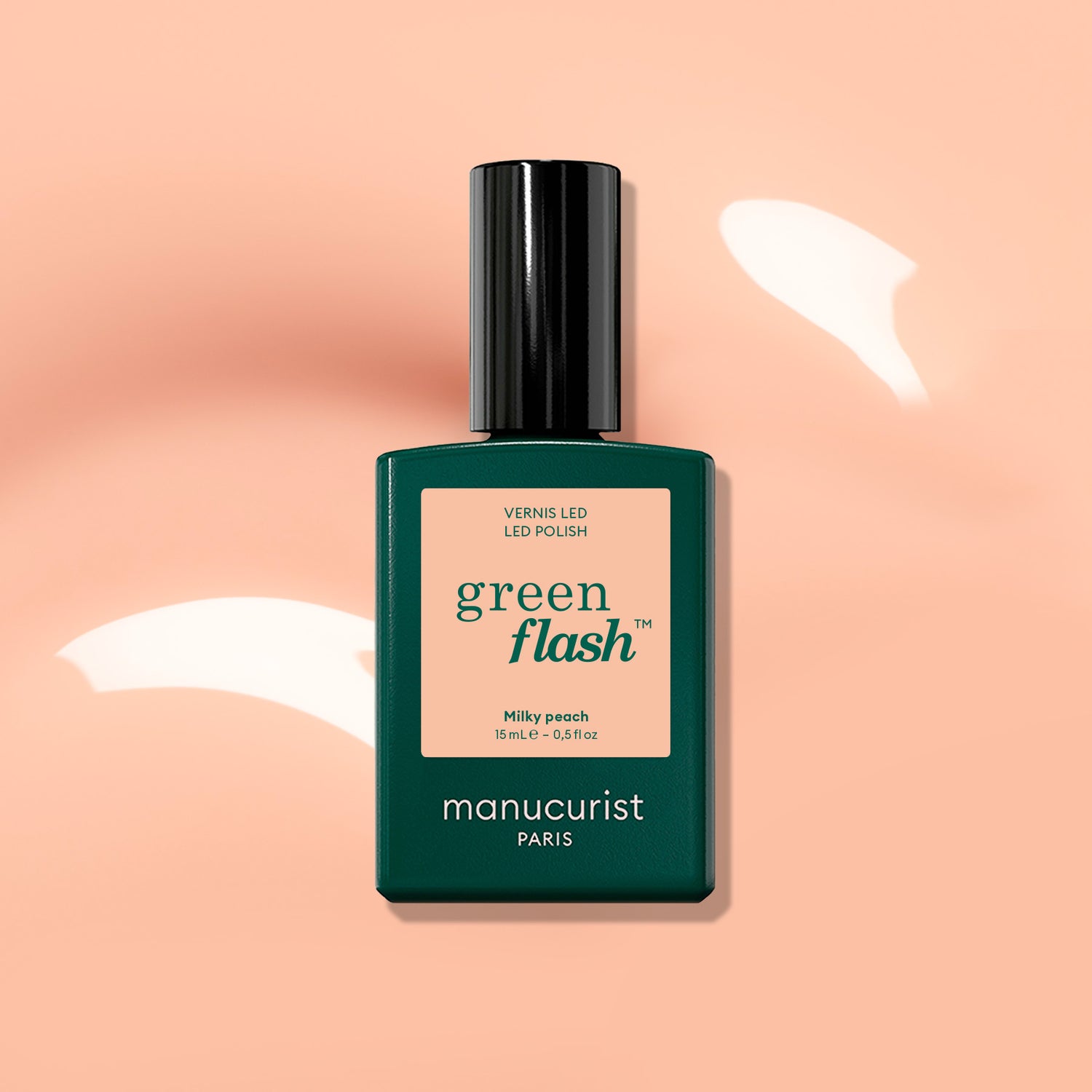 A bottle of Manucurist Milky Peach Green Flash LED polish—a milky peach gel shade with soft orange beige tones—displayed against a peach background accented by white light reflections.