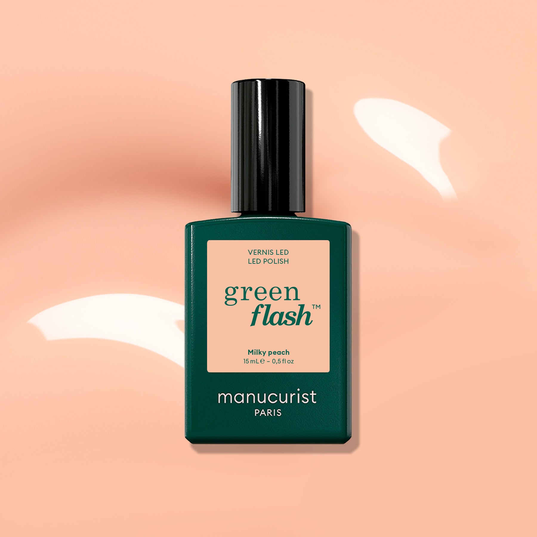 A bottle of Manucurist Milky Peach Green Flash LED polish—a milky peach gel shade with soft orange beige tones—displayed against a peach background accented by white light reflections.