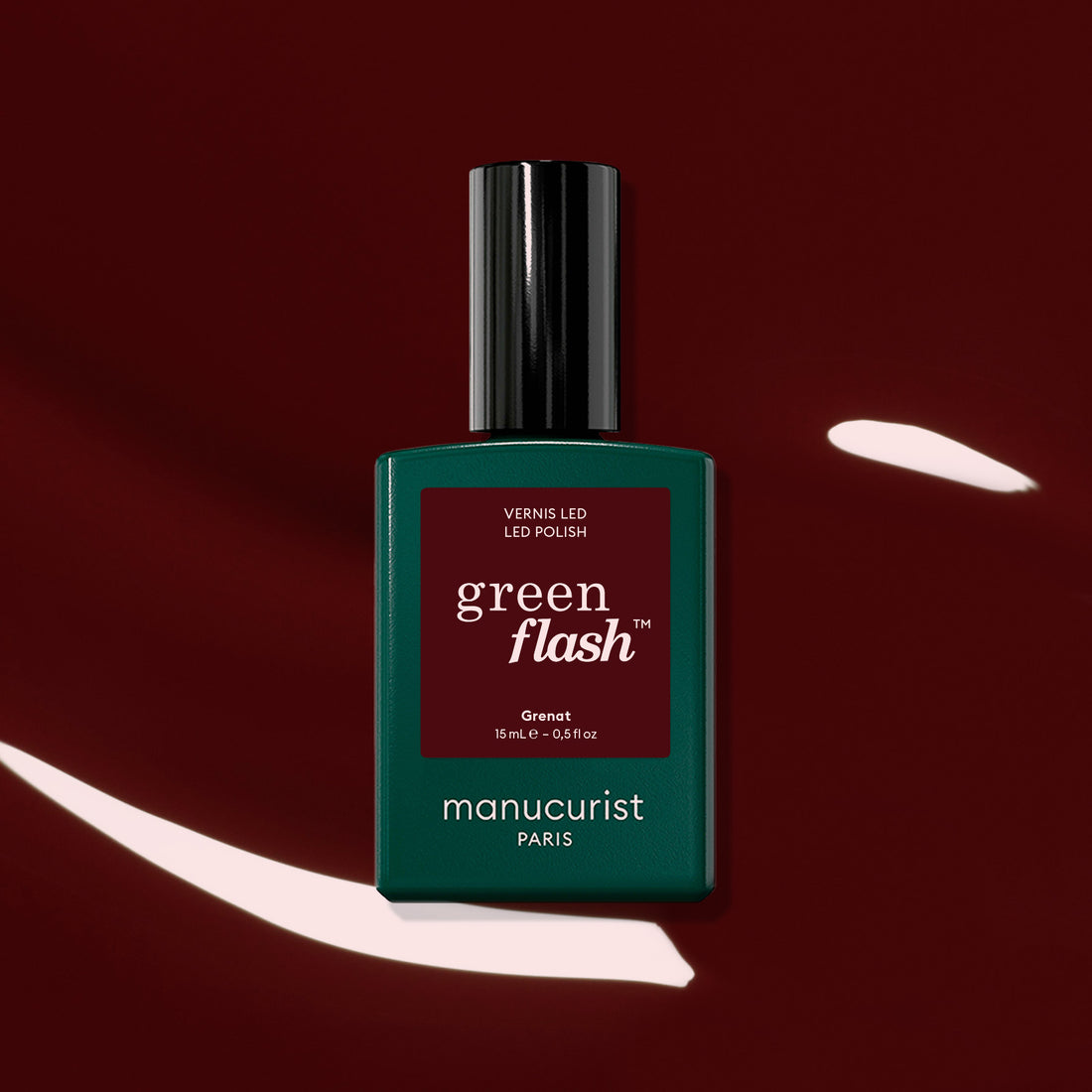 A bottle of Manucurist Green Flash LED polish in the shade Grenat is showcased against a glossy, dark maroon red background with white reflections, emphasizing the rich, earthy red tones of this gel polish.
