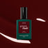 A bottle of Manucurist Green Flash LED polish in the shade Grenat is showcased against a glossy, dark maroon red background with white reflections, emphasizing the rich, earthy red tones of this gel polish.