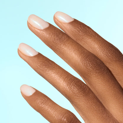 A close-up of a hand with medium brown skin shows four fingers with short, oval-shaped nails painted in Manucurist Active Plump Aqua Glazed—a shimmery, pale pink collagen polish for hydrated nails—set against a light blue background.