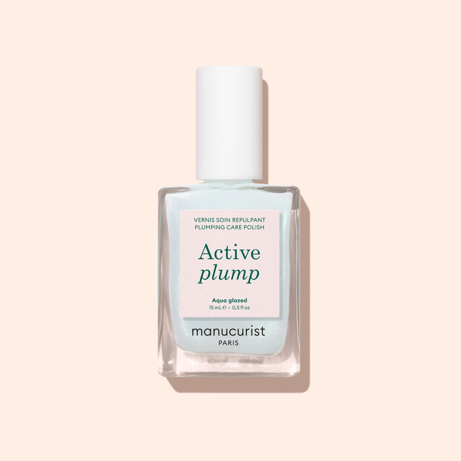 A bottle of Manucurist Active Plump Aqua Glazed nail polish with a white cap sits on a light beige background. The pale blue and white label features green and pink text, highlighting hydration for beautifully healthy nails.