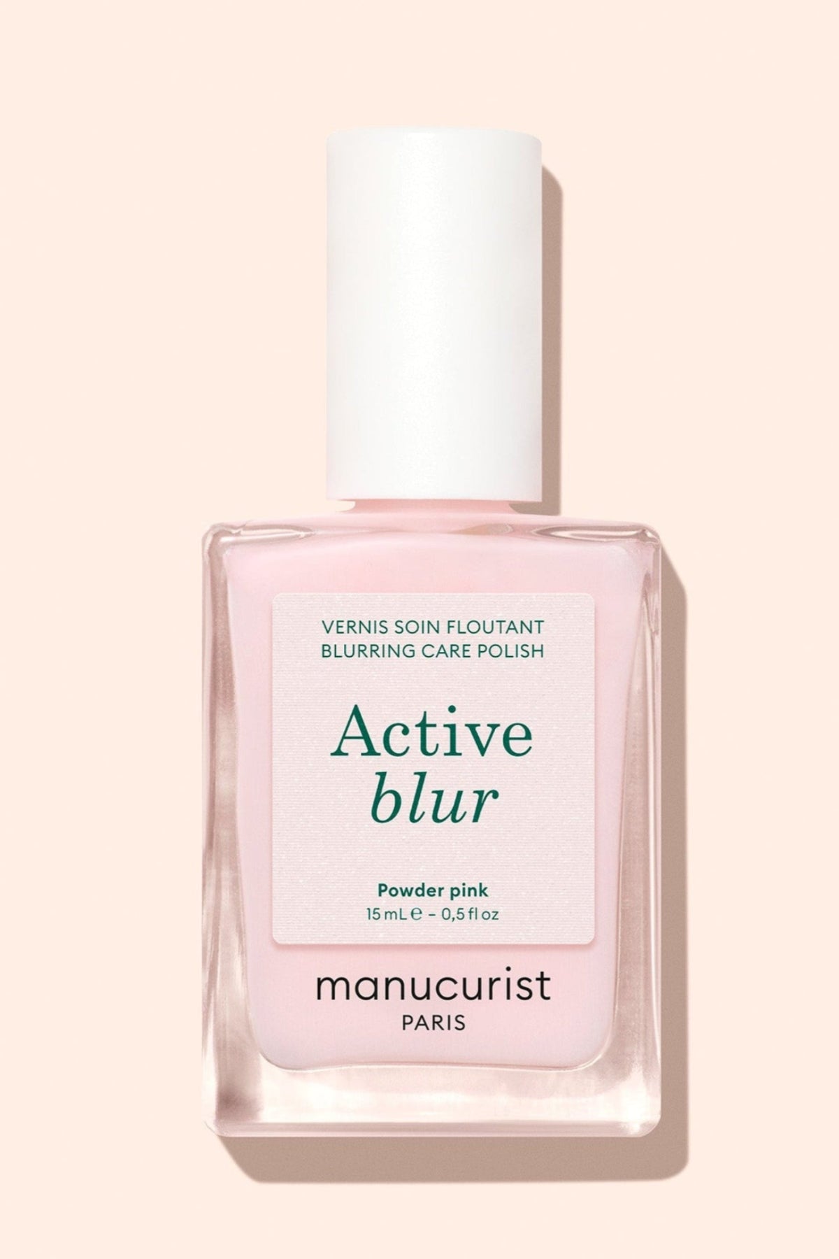 A bottle of Manucurist Paris nail polish labeled Active blur in the shade Powder pink, with a white cap and a light pink liquid inside, set against a pale pink background.
