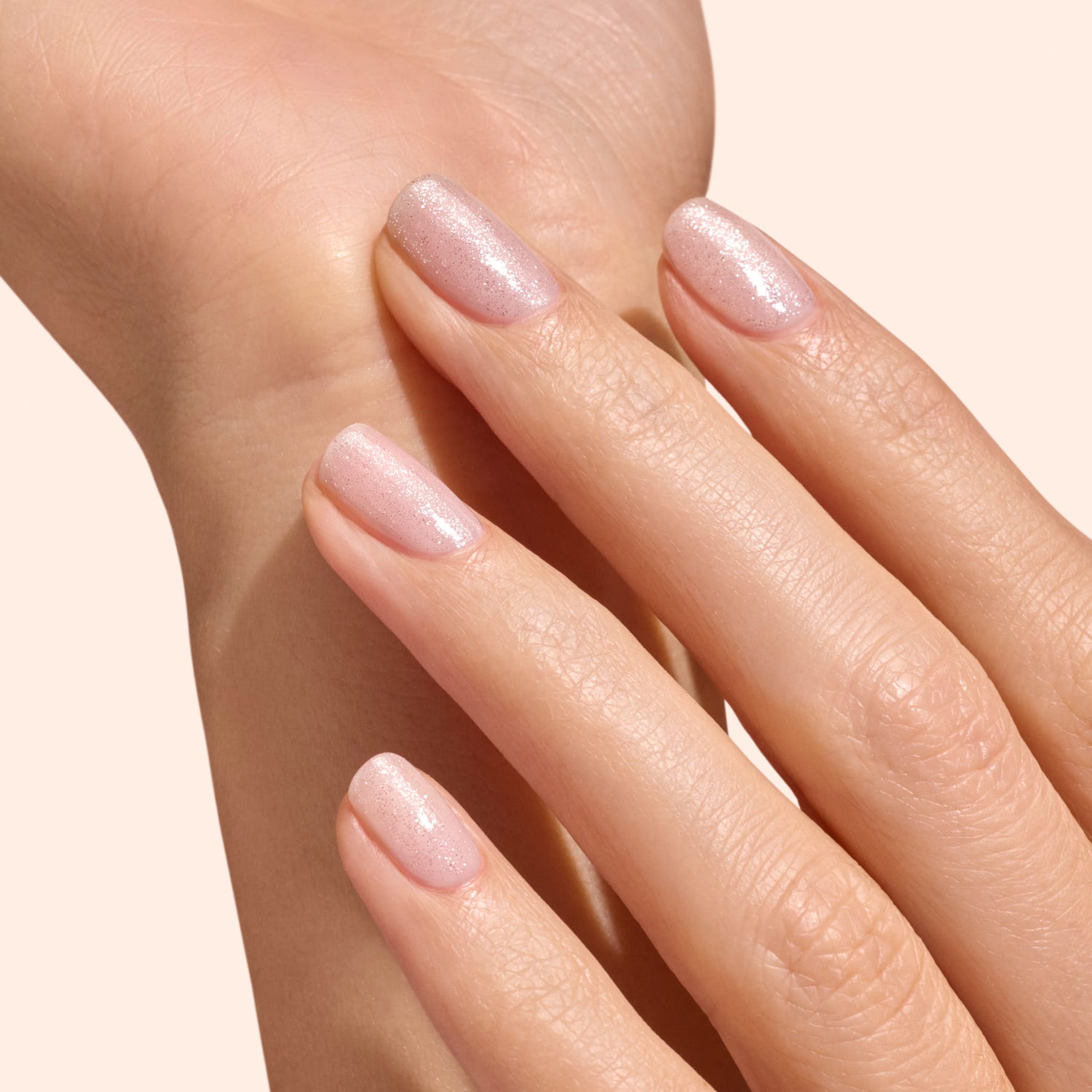 A close-up of a neatly manicured hand features shimmery pale pink nails finished with Manucurist&
