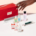 A hand reaches toward the vibrant red Ultimate Active Manicure Kit by Manucurist, surrounded by an array of nail care essentials—including nail polishes, files, a gentle cuticle remover, nourishing serums, polish remover, and professional manicure tools—all beautifully arranged on a pale surface to help you achieve healthy nails.