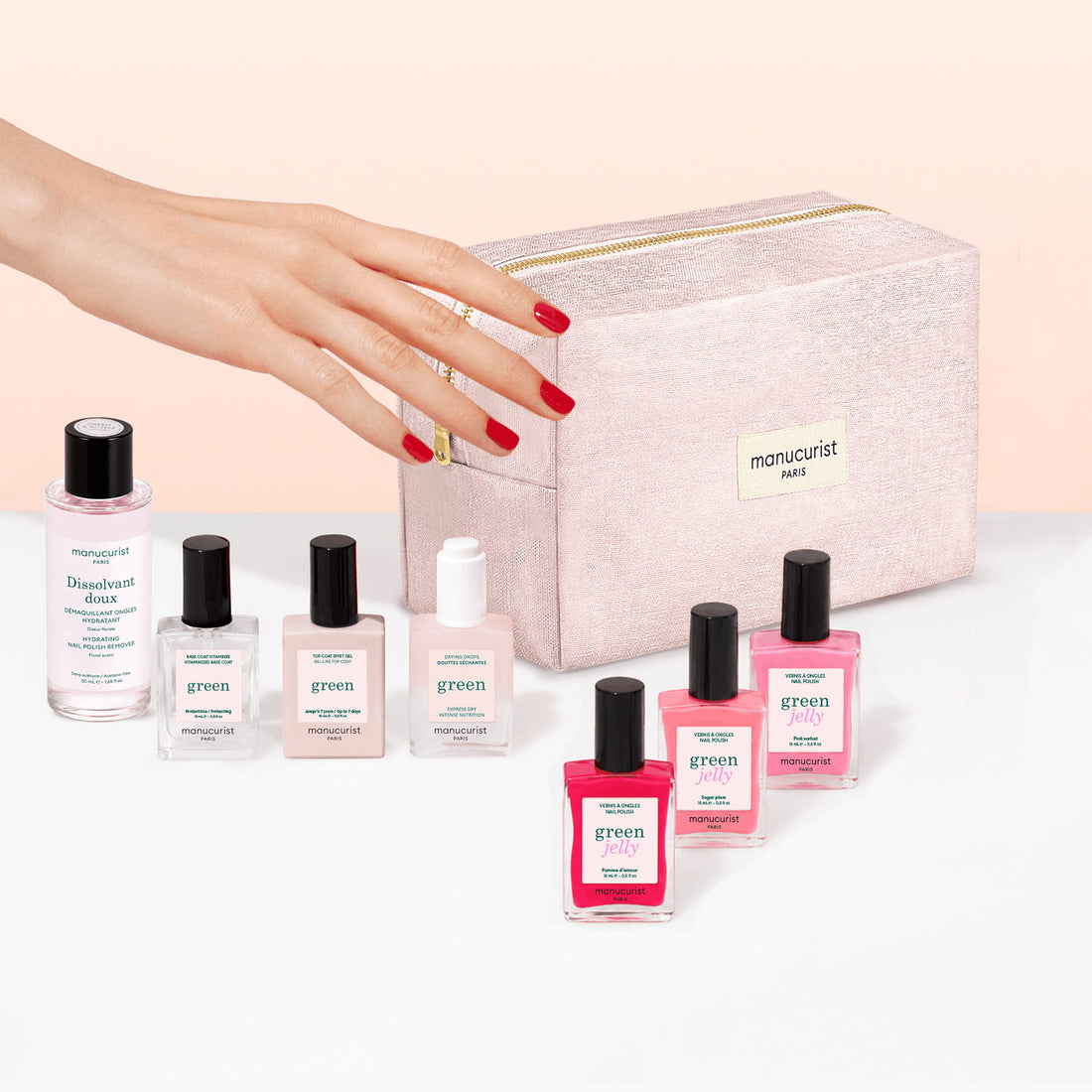 A hand with red nails reaches toward bottles of Manucurist’s Starter Kit - Jelly Nail Polish and a glittery pink manicure bag labeled Manucurist Paris. Eight plant-based nail care products are arranged neatly on a white surface.