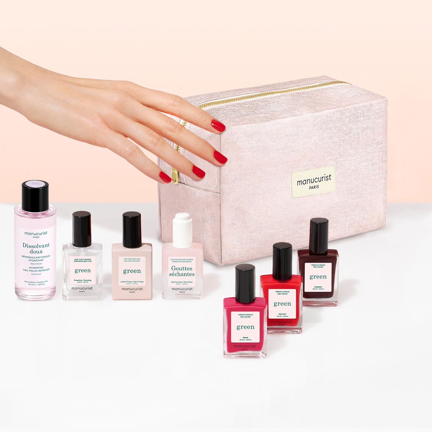 A hand with red nail polish reaches for a pink makeup bag, surrounded by bottles of nail polish remover and an assortment of Manucurist Starter Kit plant-based nail polishes, including options for a green manicure and gel effect manicure.