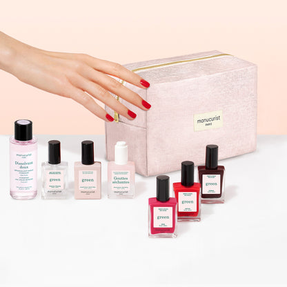 A hand with red nail polish reaches for a pink makeup bag, surrounded by bottles of nail polish remover and an assortment of Manucurist Starter Kit plant-based nail polishes, including options for a green manicure and gel effect manicure.