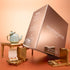 A large Manucurist Green™ Gift Set Holiday box in rose gold rests on a peach surface, accompanied by a blue teapot, gold jewelry boxes, and small beauty items, creating a luxurious and elegant display.