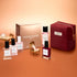 The Manucurist Green™ Discovery Kit Gift Set, featuring naturally derived nail polishes, remover, and a red pouch, is displayed with miniature furniture on a peach background. A gold Manucurist box sits in the back, making this set an ideal holiday gift.