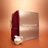 An Active™ Gift Set Holiday by Manucurist, featuring a maroon pouch and a metallic box labeled “Manucurist Paris,” is displayed on an orange surface, accompanied by a small white porcelain creamer decorated with flowers in front.