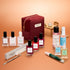 The Manucurist Green™ Ultimate Kit Gift Set is elegantly displayed, featuring a burgundy manicure bag surrounded by gel effect polish, naturally derived nail polishes, treatments, nail files, and professional manicure tools. In the background, a miniature golden table and chair with a teapot and cup add charm to the scene. All products are thoughtfully arranged—ideal for creating an at-home manicure experience.