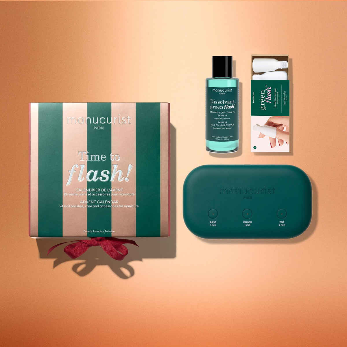 Four Manucurist manicure products are displayed on a peach background: the “Advent Calendar Time to Flash!” gift box with a red ribbon, a bottle of nail polish remover, a green Green Flash gel polish manicure box, and a green Manucurist LED nail lamp with labeled buttons.