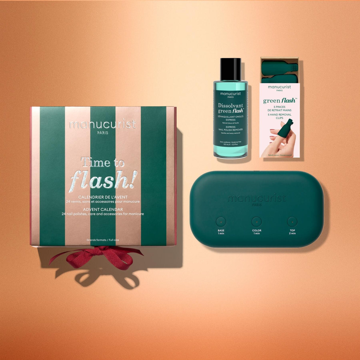 Four Manucurist manicure products are displayed on a peach background: the “Advent Calendar Time to Flash!” gift box with a red ribbon, a bottle of nail polish remover, a green Green Flash gel polish manicure box, and a green Manucurist LED nail lamp with labeled buttons.