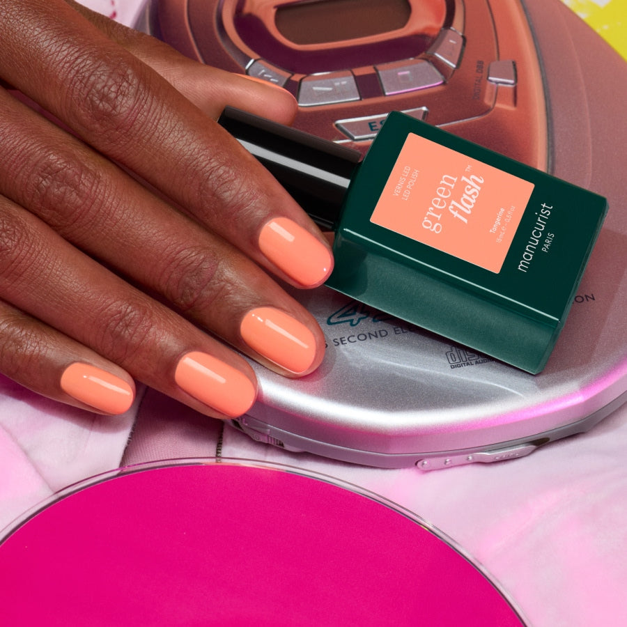 A hand with glossy, nineties-inspired nails rests on a portable CD player, next to a bottle of Manucurist&