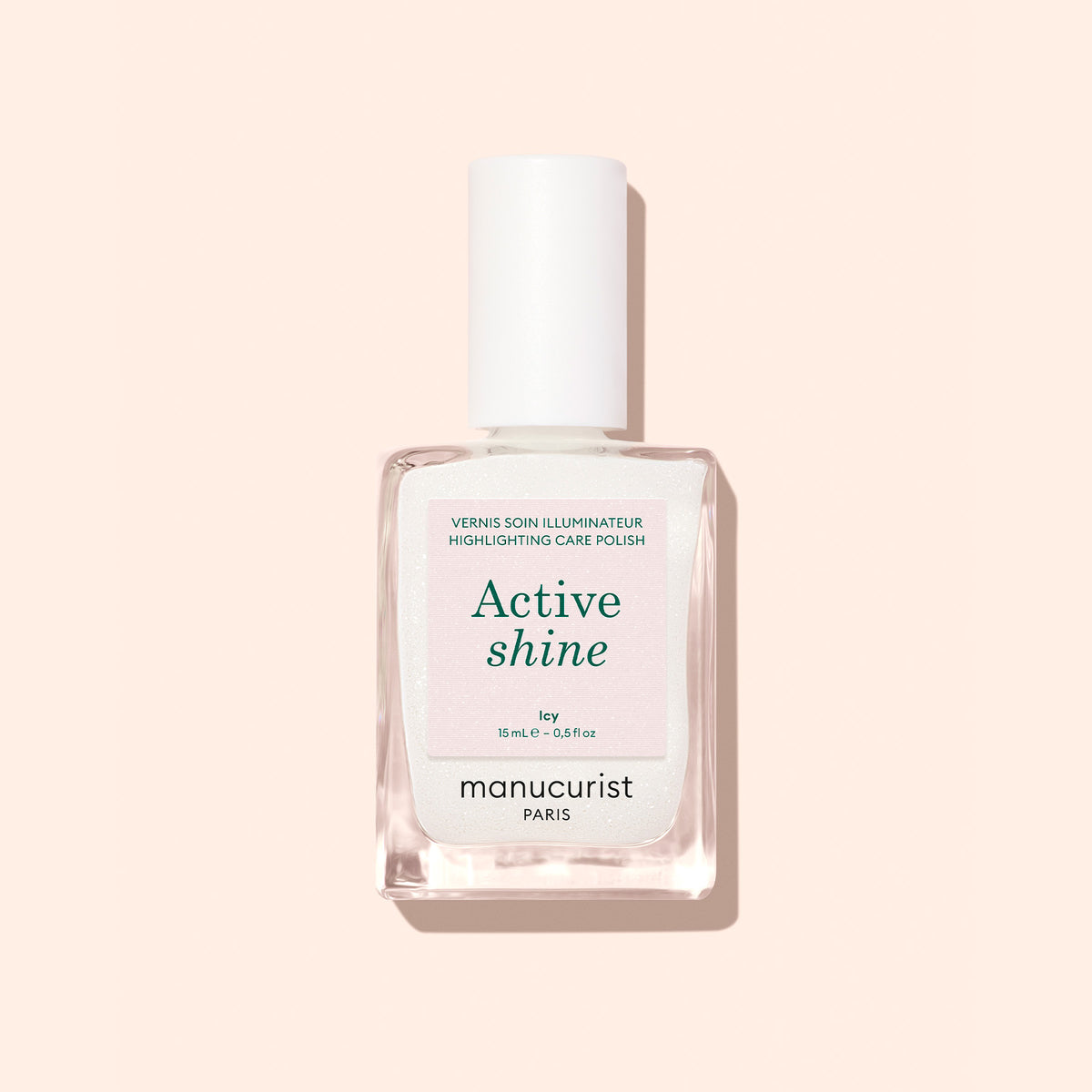 Un flacon en verre transparent de vernis illuminateur Active™ Shine Icy de Manucurist, avec un bouchon blanc, photographié sur un fond pêche pâle.