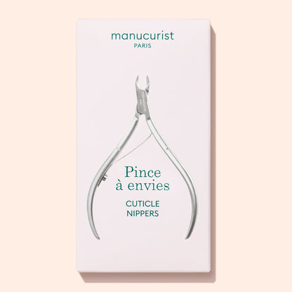 Silver metal stainless steel Manucurist Cuticle Clippers centered on a white rectangular product box with the text Pince à envies and CUTICLE NIPPERS printed below.
