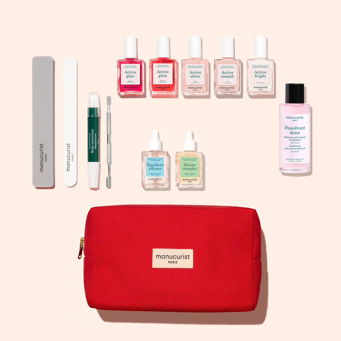 The Manucurist Super Ultimate Active Manicure Kit is a comprehensive nail care set featuring manicure tools and products for healthy nails, including nail files, cuticle remover, six bottles of nail polish, three nourishing care oils, remover, and a stylish red manicurist pouch—all neatly arranged on a beige background.