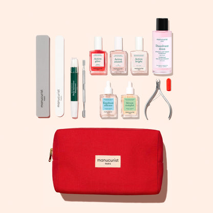 The Manucurist Ultimate Active Manicure Kit is a red pouch that contains a complete nail care set—including nail files, a cuticle pen, a cuticle pusher, nail polishes, polish remover, cuticle remover, nail clippers, and a matching red-cap accessory—all beautifully arranged on a light background to maintain healthy nails.