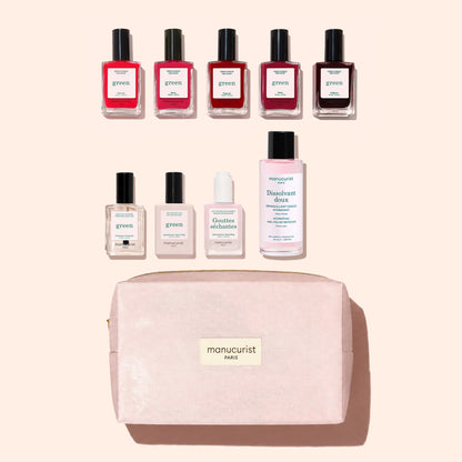 Nine manicure products from Manucurist’s Super Starter Kit—including seven bottles of plant-based nail polish, one remover, and one drops—are arranged above a pink zippered makeup bag labeled “manucurist PARIS” on a light pink background.