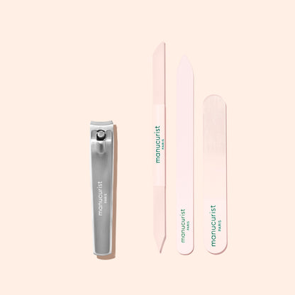 A Manucurist Nail Clipper in silver and three pastel pink nail files, each bearing the Manucurist brand, are arranged neatly on a light beige background.