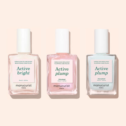 Three bottles of Manucurist nail polish—Active Bright, Active Plump Pink Glow, and Active Plump Aqua Glazed—stand against a light pink background, delivering hydrated nails with a subtle pearly finish.