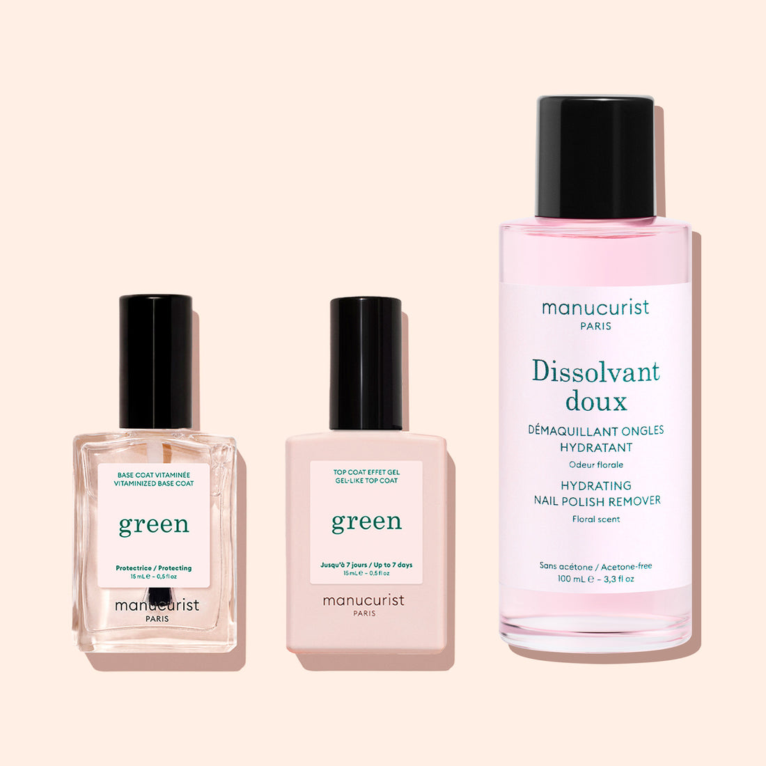 Three manicure products: two square bottles labeled Manucurist Green—one featuring the Vitaminized Base Coat Green™, a nail polish base coat with innovative KeraHCE+ technology to strengthen nails—and a tall, round bottle labeled Manucurist Dissolvant Doux containing pink liquid, all arranged on a light pastel background.