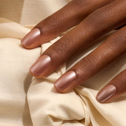 A hand with medium brown skin rests on a cream-colored fabric. The fingernails are neatly manicured and painted with Manucurist’s Sandstone polish, a shimmering latte brown that gives them an elegant, glossy finish.