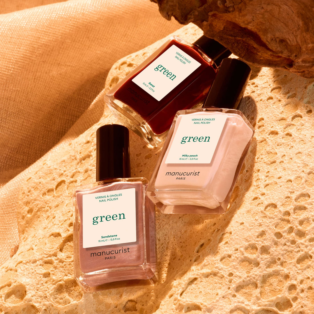 Three bottles from the Manucurist Curated Trios collection are arranged on a textured stone surface in warm lighting, perfectly showcasing expertly selected color palettes inspired by the latest nail trends.