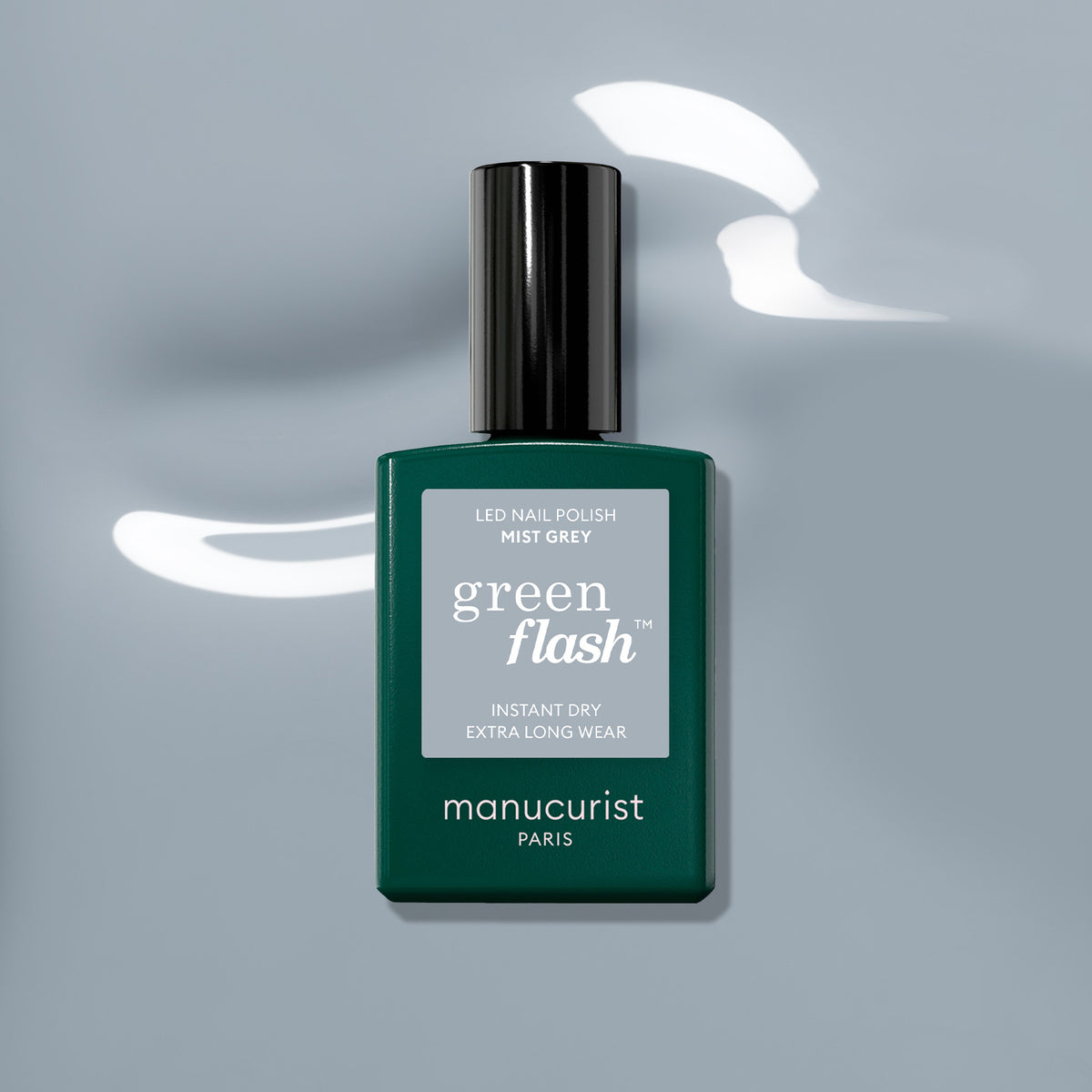 A bottle of Manucurist Mist Grey Green Flash LED gel polish sits on a glossy light grey surface, with reflections visible around its dark green rectangular base and black cap.