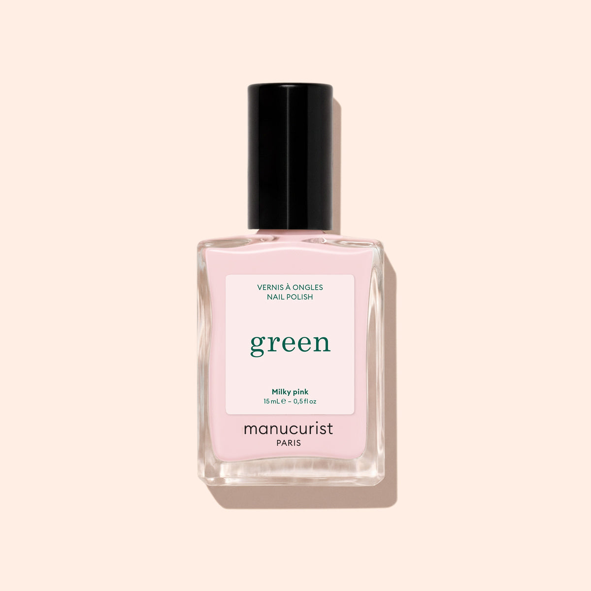 Un flacon de vernis à ongles Manucurist Milky Pink avec un bouchon noir est présenté sur un fond beige.