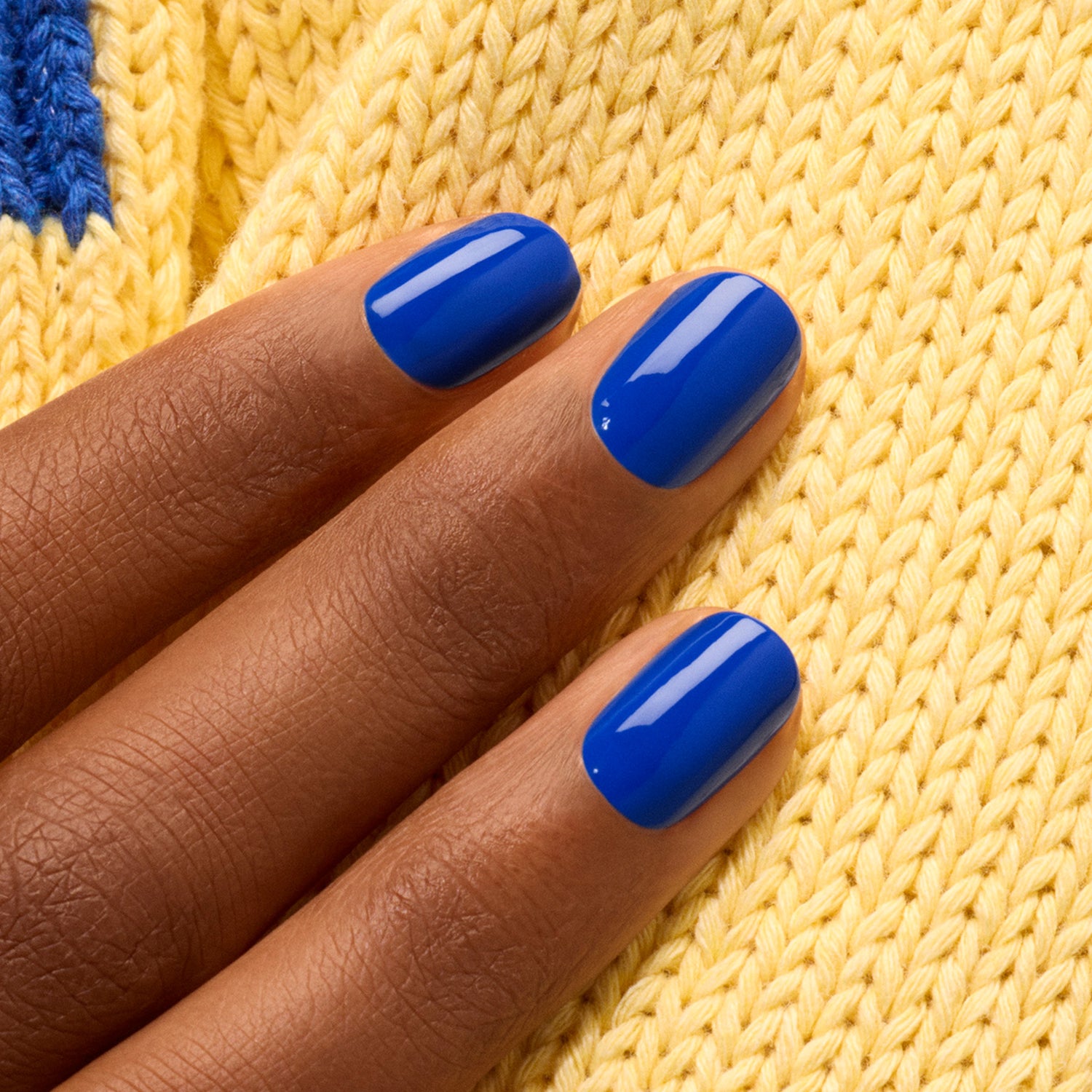 A hand with medium brown skin and short, neatly manicured nails painted in Manucurist&