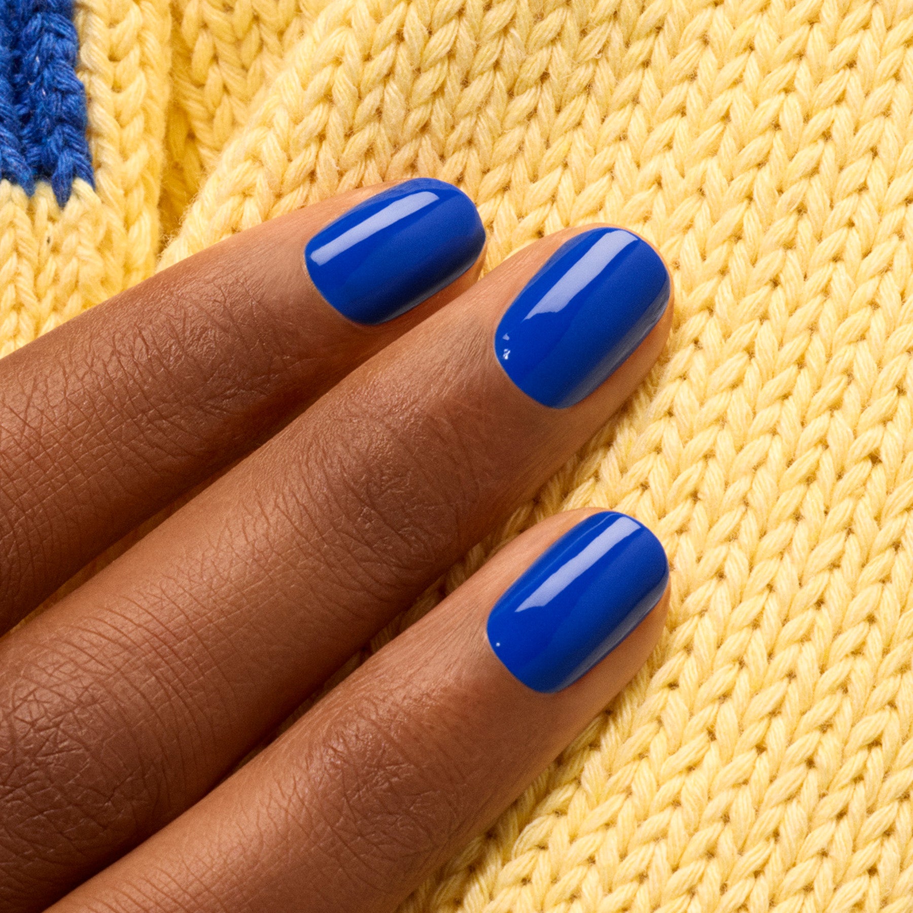 A hand with medium brown skin and short, neatly manicured nails painted in Manucurist&