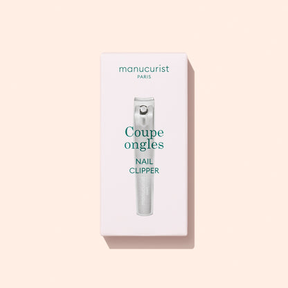 A box of Manucurist Nail Clipper, a precision nail cutter and must-have manicure tool, featuring the text “Coupe ongles Nail Clipper” on a light pink background.