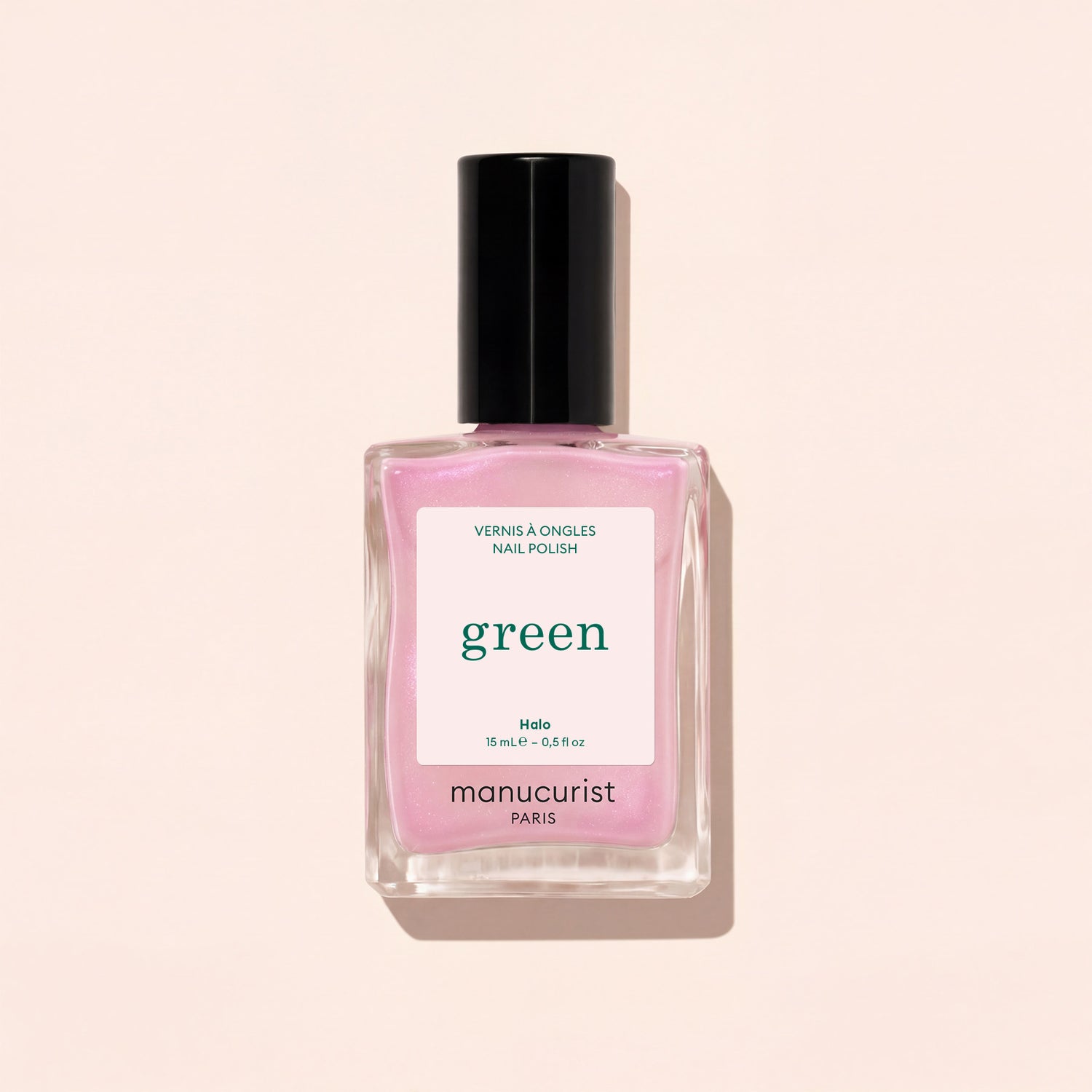A square glass bottle of Manucurist nail polish in the shade Halo, a milky mauve color with a black cap, is shown against a light beige background.