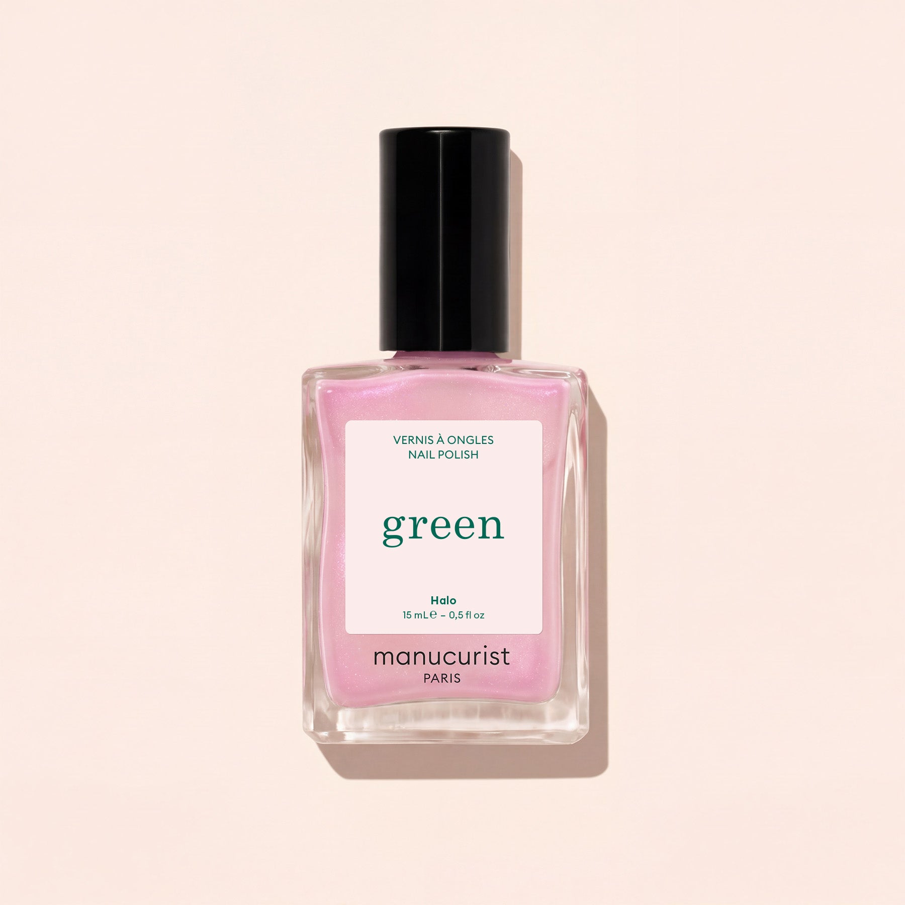 A square glass bottle of Manucurist nail polish in the shade Halo, a milky mauve color with a black cap, is shown against a light beige background.