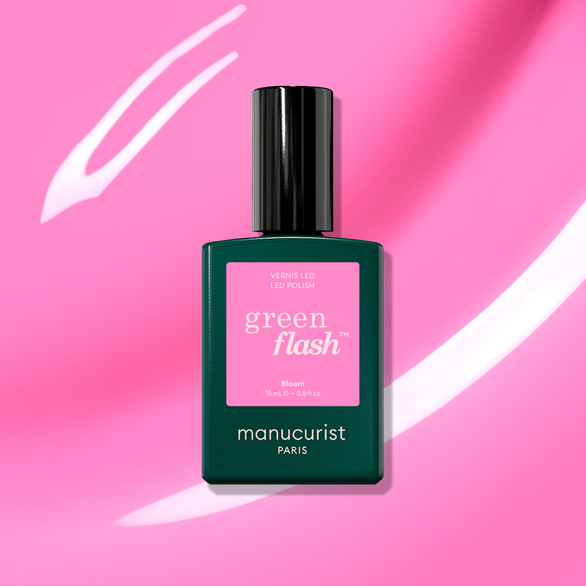 Un flacon de vernis gel Bloom de Manucurist repose sur un fond rose strié de blanc. Le flacon vert foncé arbore une étiquette rose portant les mentions « green flash » et « Bloom », pour un look intensément magnétique.