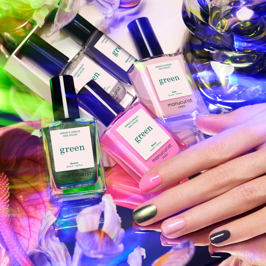 A hand with multicolored nails rests beside five Manucurist Curated Color Collections bottles, surrounded by vibrant flowers and swirling lights, highlighting the latest nail trends and curated palettes for stunning manicures.