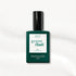 A bottle of Manucurist Bliss gel polish, featuring a dark green label and black cap, is displayed on an iridescent white, subtly sparkling surface.