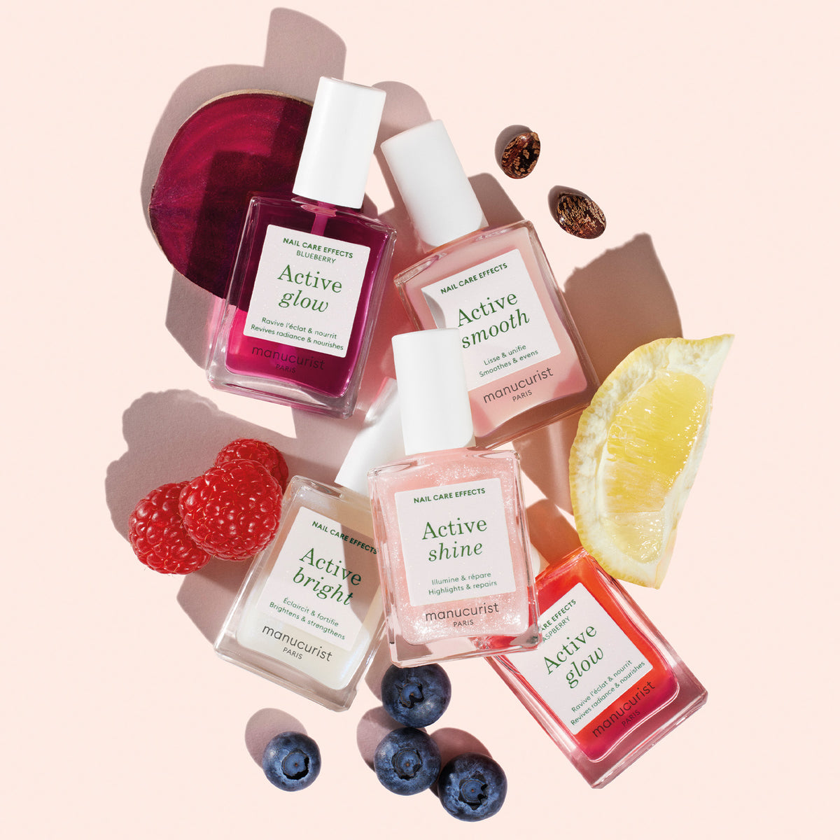 Cinq flacons du Manucurist Active Discovery Kit sont présentés sur un fond rose pâle, entourés de framboises fraîches, de myrtilles, de citron et de betterave.