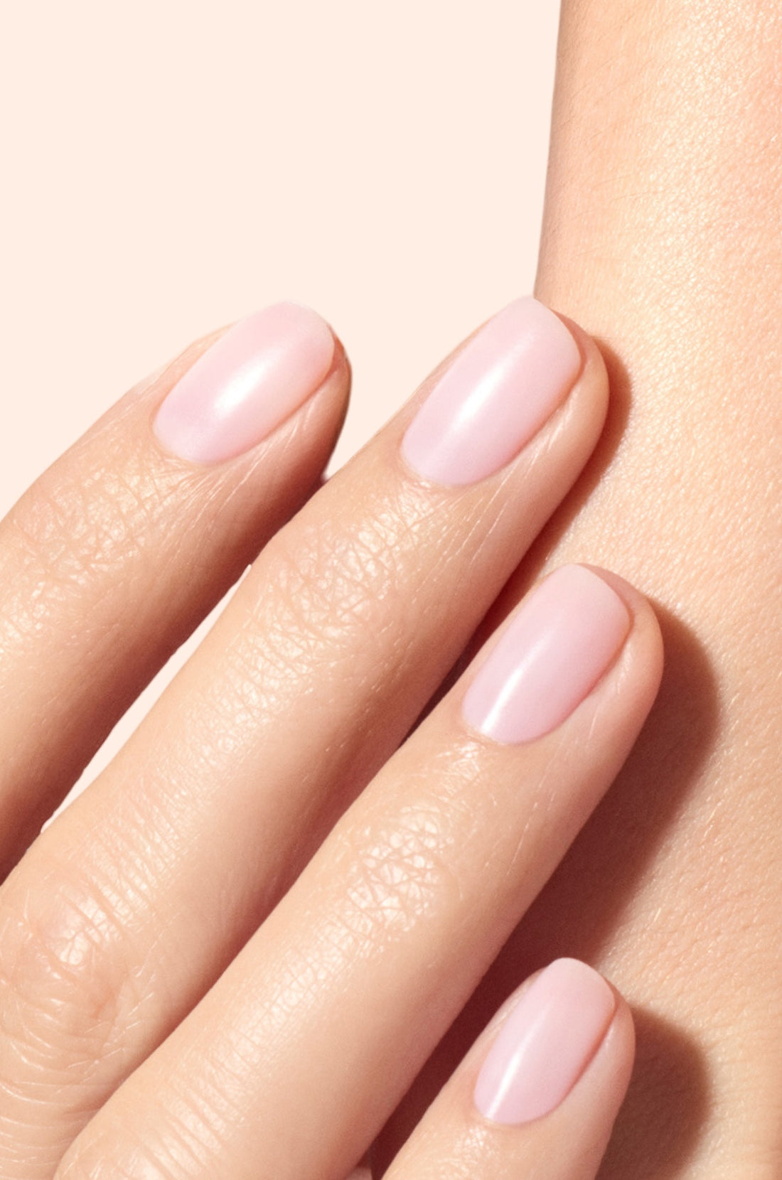 A close-up of a hand with neatly manicured nails painted in a soft, pale pink color, set against a light beige background.