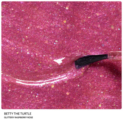 A close-up of a nail polish brush applying glittery raspberry rose nail polish with sparkling flecks. Text at the bottom reads: Manucurist, Petite Manucurist Trio—a natural origin children’s nail polish set perfect as a holiday gift.