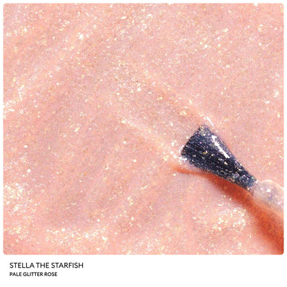 A nail polish brush applies a shimmering, pale rose-gold glitter polish onto a smooth surface. The Petite Manucurist Trio by Manucurist features Stella the Starfish: Pale Glitter Rose—a children’s nail polish of natural origin, perfect as a sparkling holiday gift.