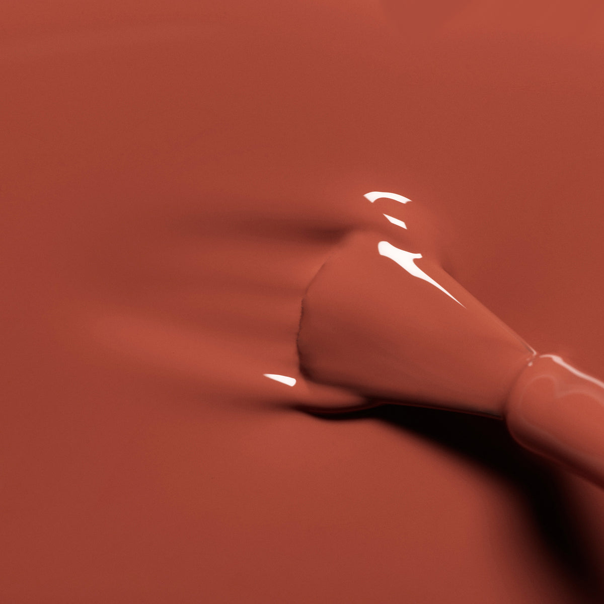 Gros plan d’un pinceau de vernis à ongles étalant un vernis à ongles Manucurist Green Flash Brique rouge brique brillant sur une surface lisse.