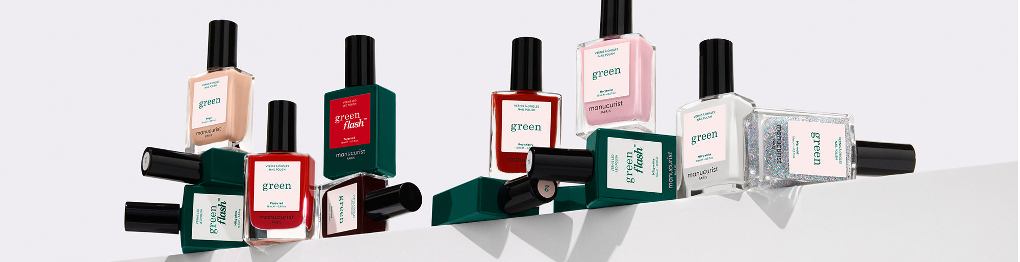 Several bottles of nail polish in various colors, including red, green, pink, and clear, are arranged on a white surface. Some bottles stand upright, while others are lying on their sides.