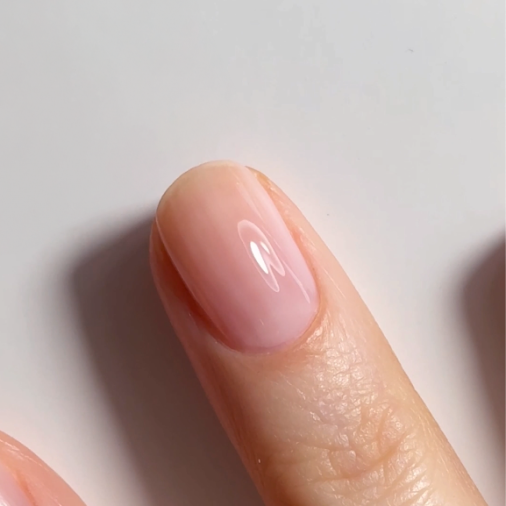 A close-up of a hand showing neatly manicured fingernails with a natural, glossy, light pink polish. The nails are smooth and well-shaped against a plain white background.