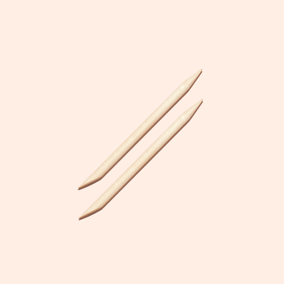 Two Manucurist US Wooden cuticle sticks (x2), each featuring pointed and angled ends, are placed parallel to each other on a pale beige background.