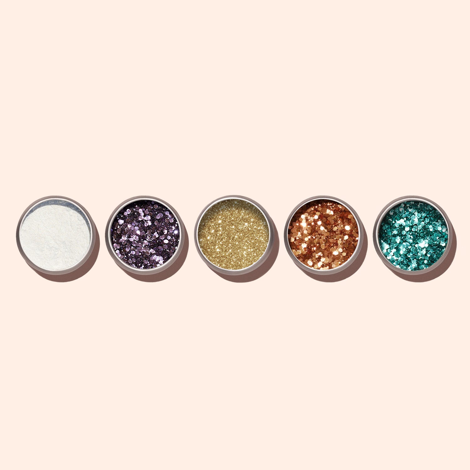 Five small round containers of Manucurist’s Lilac Biodegradable Glitter, each in white, purple, gold, copper, and teal—perfect for nail art—are arranged in a row on a light beige background.